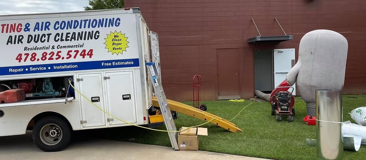 Air conditioning service truck parked by a brick wall, with a worker kneeling near equipment and piping.
