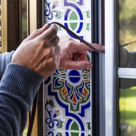 Hands applying black sealant to a colorful decorative glass window frame