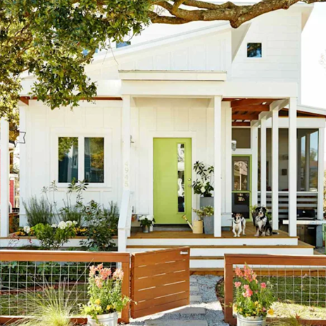 White house with lime-green door, porch plants, and two dogs sitting at the entrance
