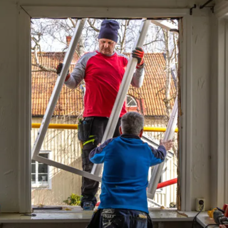 Two workers installing a white window frame in a doorway opening