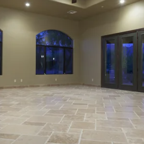 Empty tiled living room with arched window, beige walls, and dark glass double doors at dusk