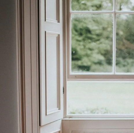 Open white window with soft green trees visible outside and light entering the room