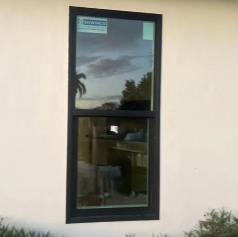 Black-framed window in a beige wall reflecting trees and sky.