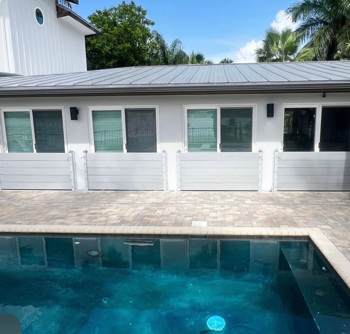 Backyard pool in front of a white house with flood barriers