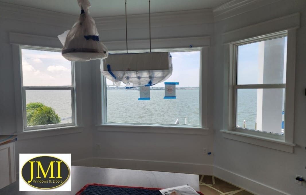 A bright room featuring a bay window with a scenic water view, featuring a light fixture wrapped in protective plastic.