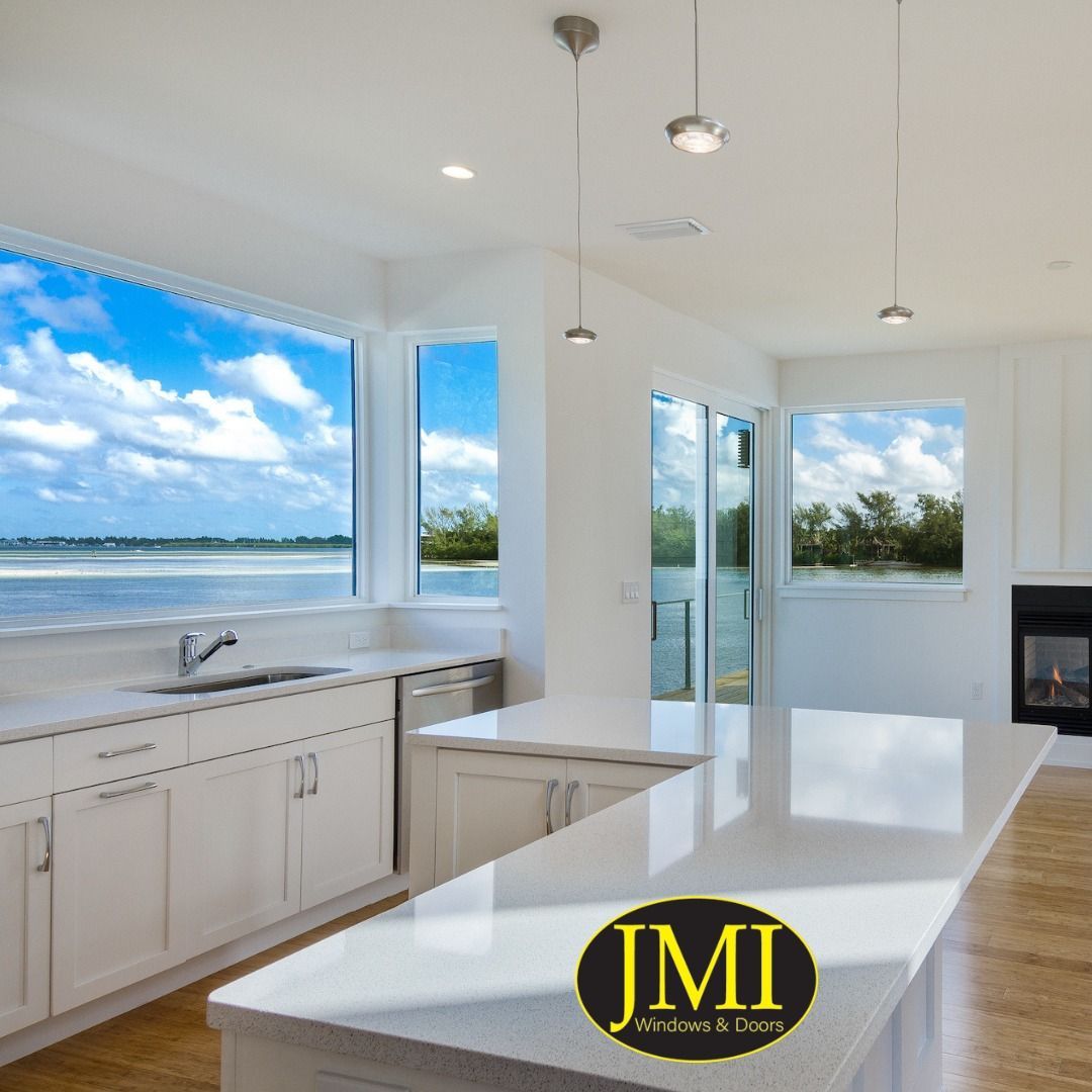 A modern, white-cabinet kitchen with a quartz island and expansive windows overlooking a calm coastal water view.