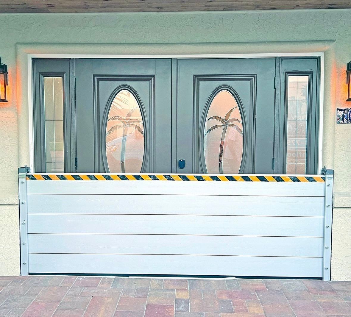 Double front doors with oval glass panels behind a white flood barrier