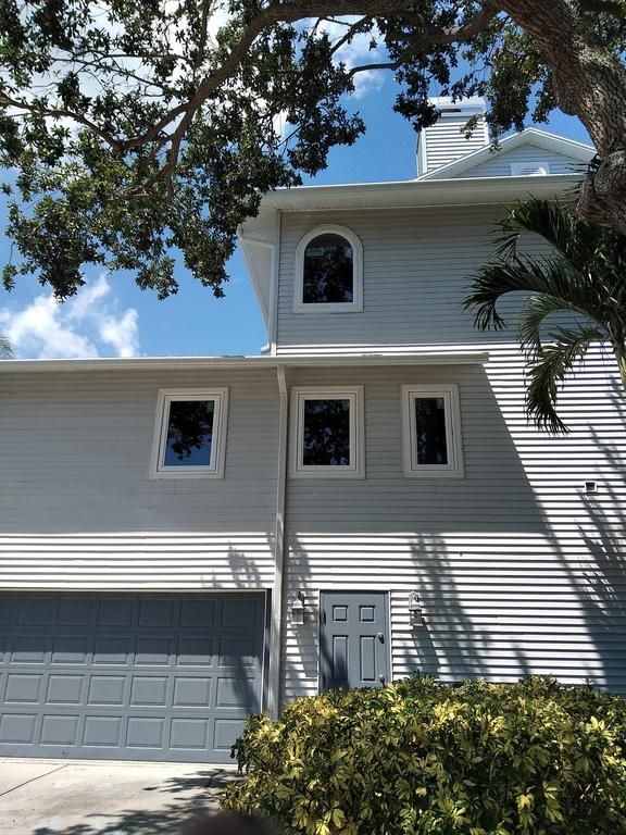White two-story house with gray garage, front door, and trees against a blue sky
