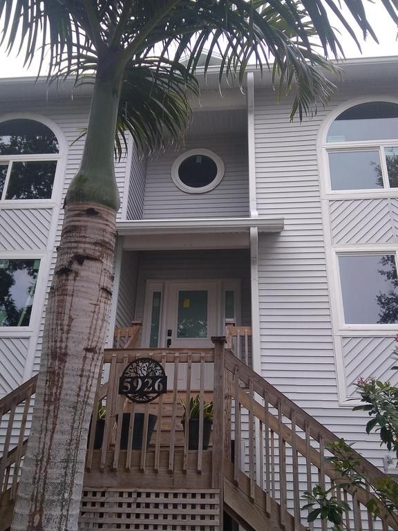 Front view of a white apartment building with a wooden stairway and palm trees in front