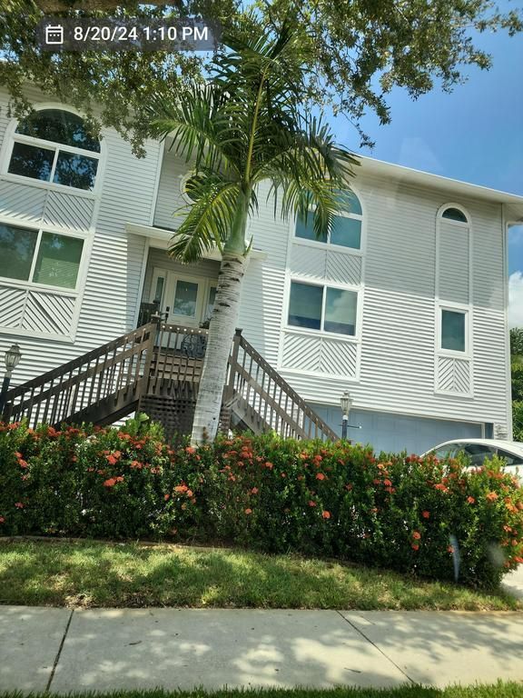 Apartment building with stairs, palm trees, and flowering bushes by the sidewalk
