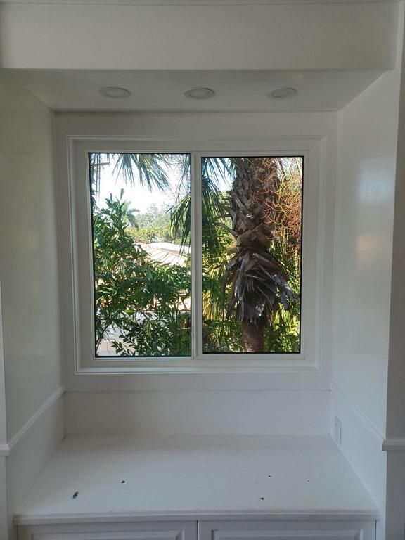 White room alcove with a window overlooking palm trees and greenery outdoors