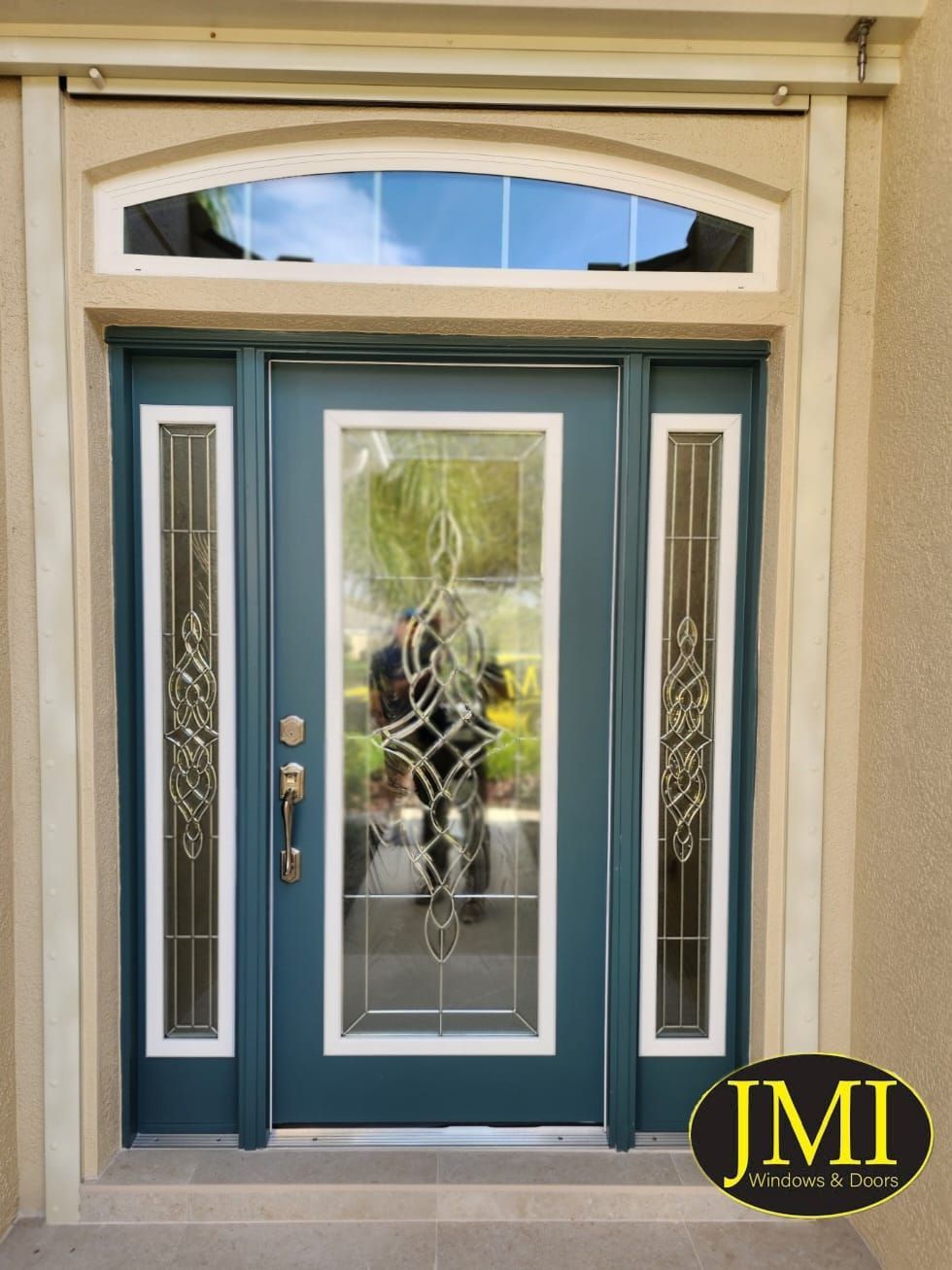 A dark teal front door with a decorative glass insert, matching side windows, and an arched transom window above.
