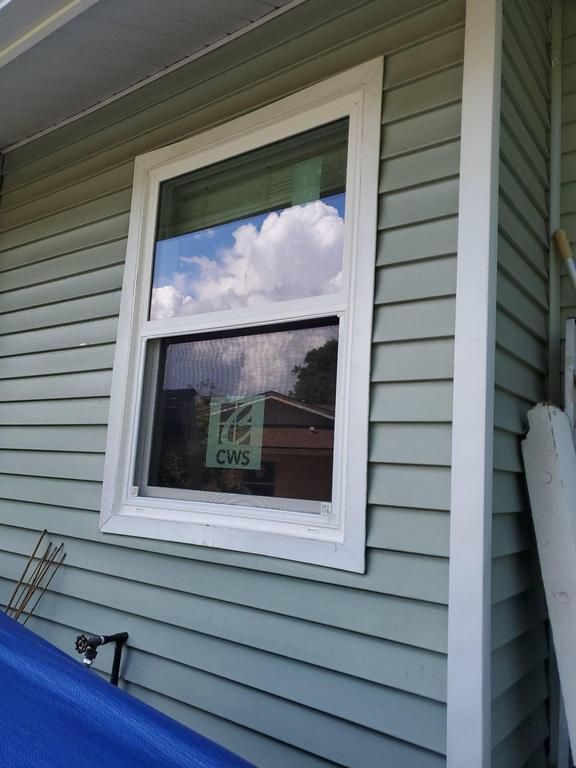White-framed window on light green house siding, reflecting clouds and a nearby roof
