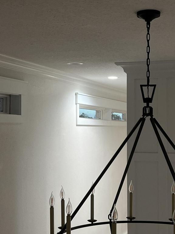 Black chandelier hanging from a ceiling in a bright white room with a small high window