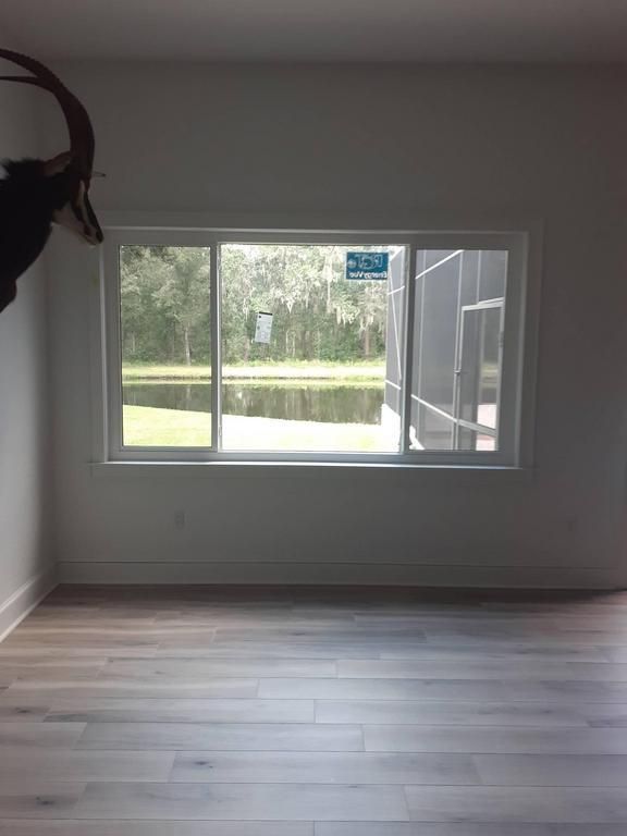 Empty room with light wood floor, gray walls, and a large window overlooking greenery