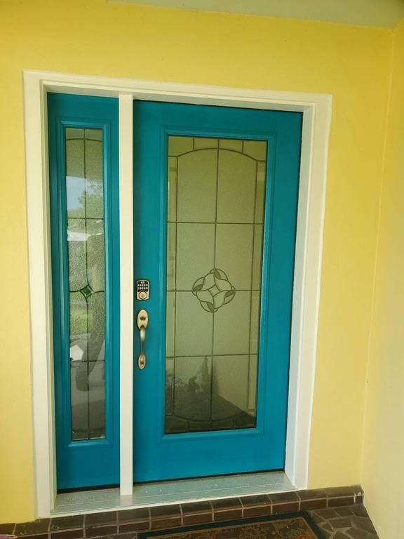 Teal front door with frosted glass panels framed by white trim on a yellow exterior wall