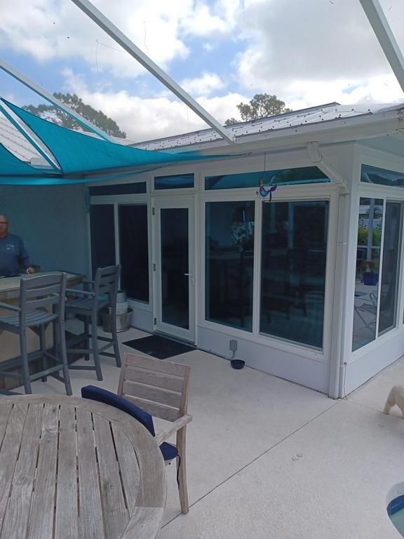 Patio with white-framed glass doors, outdoor table and chairs, under a blue shade