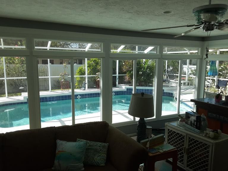 Living room with large windows overlooking a bright backyard pool and patio