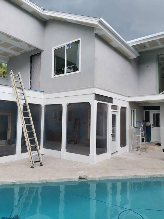 Gray two-story house with large windows beside a pool, with ladders leaning against the exterior
