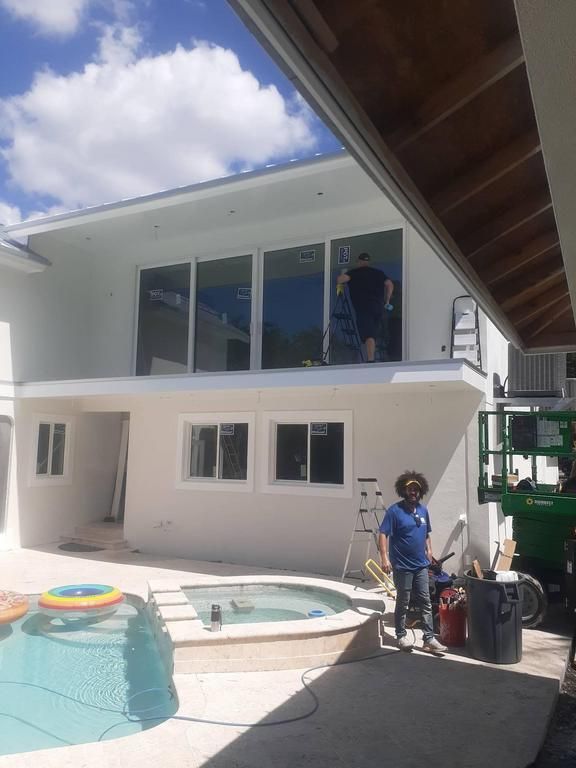 Backyard with a modern white house, pool, and workers on a balcony and by the pool