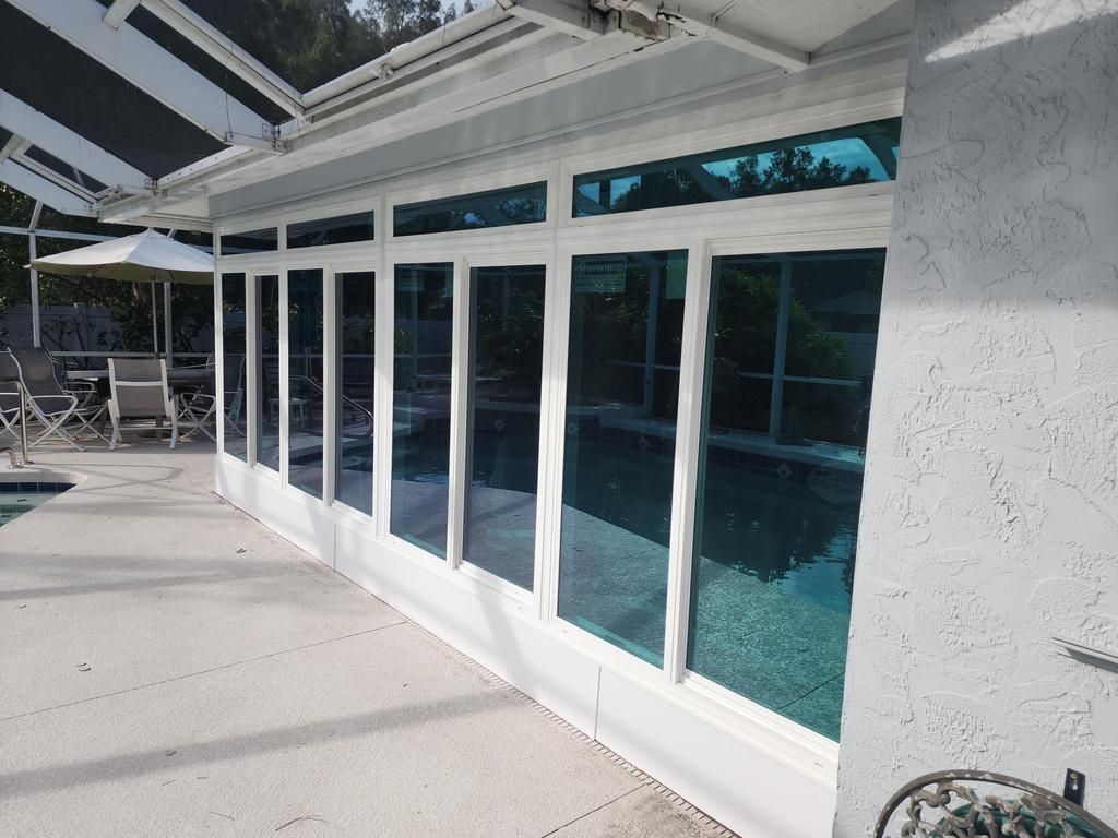 White-trimmed glass enclosure beside a pool patio under bright sunlight