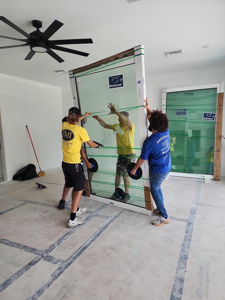 Three people install a glass panel in a bright room