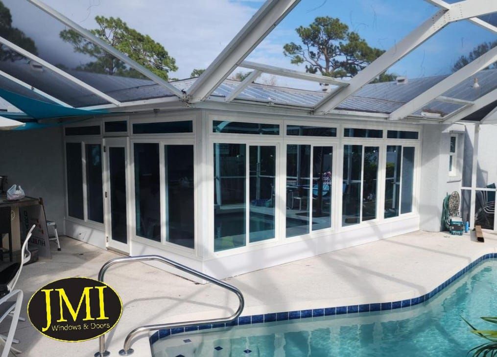 A sunroom addition with white frames and sliding glass doors, situated on a patio beside a swimming pool under a screen.