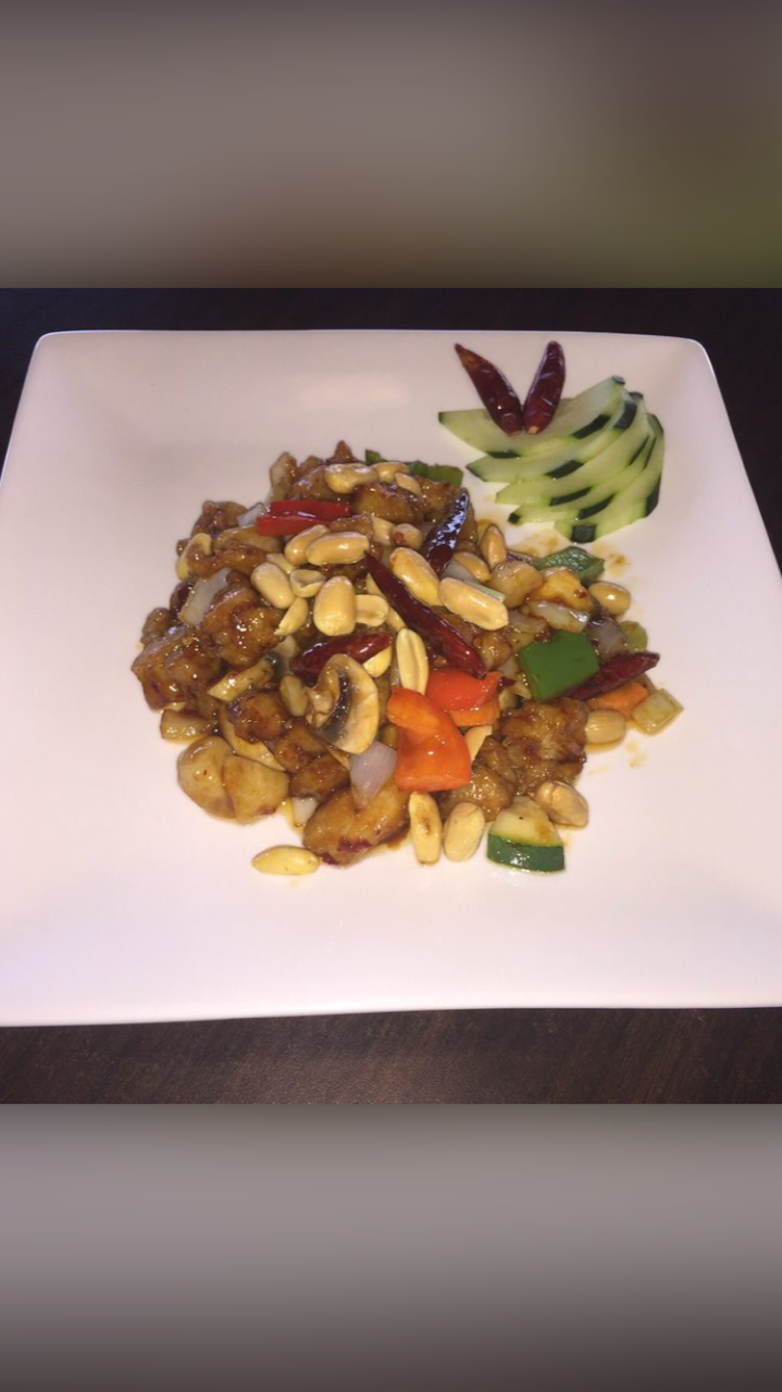 A plate of food with vegetables and peanuts on a table.