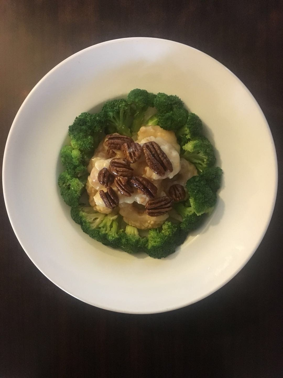 A white bowl filled with broccoli and pecans on a table