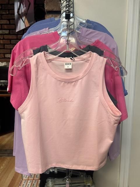 A pink tank top is hanging on a rack with other tank tops