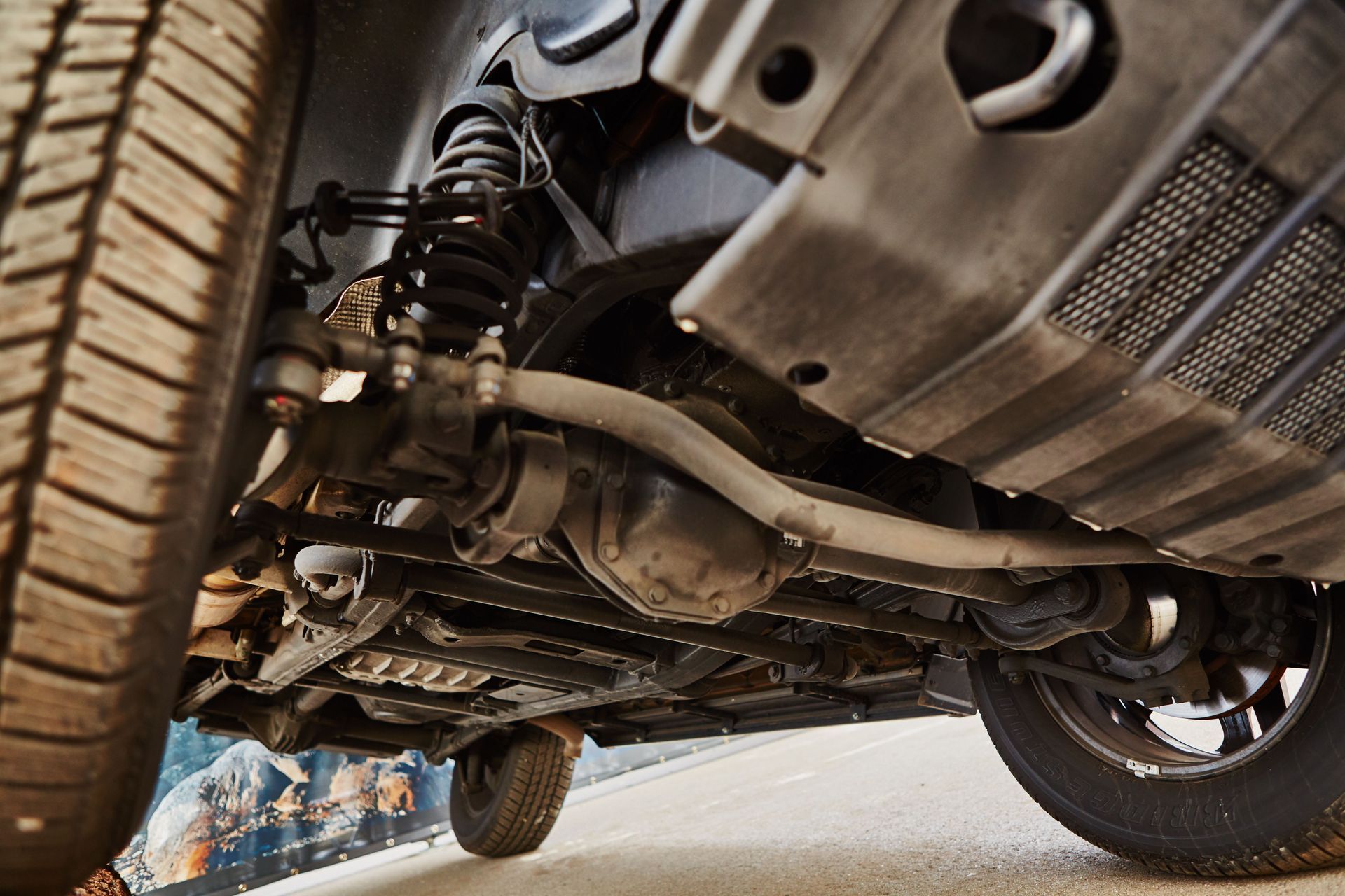 Underside of a vehicle, showing suspension, axles, and tires, with black and gray components in a low angle shot.