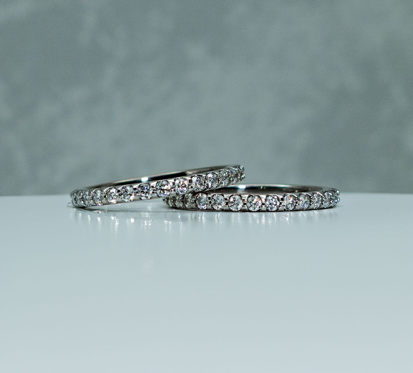Two silver diamond bands resting on a pale blue surface