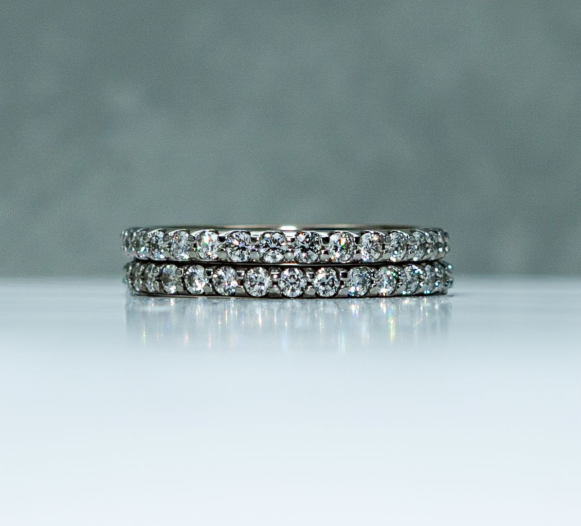 Two diamond-studded rings stacked on a reflective surface against a gray background