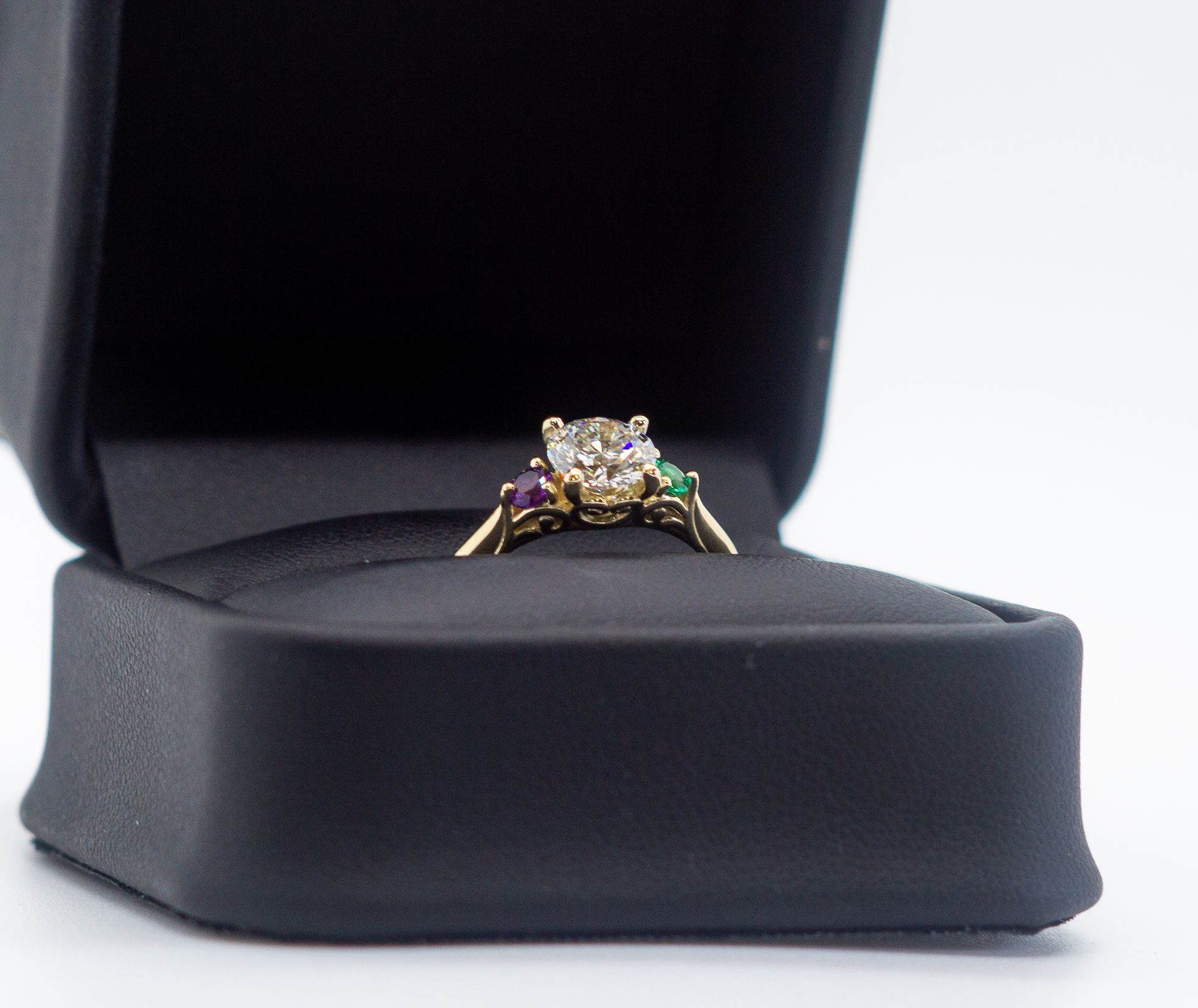 Gold ring with a central diamond and colored side stones displayed in a black jewelry box