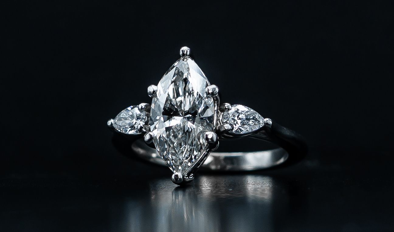Marquise-cut diamond engagement ring with side stones on a dark reflective surface