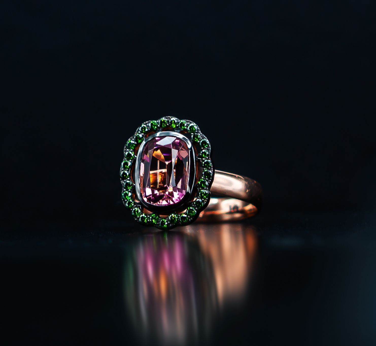 Emerald and purple gemstone ring on a reflective black surface, lit dramatically.