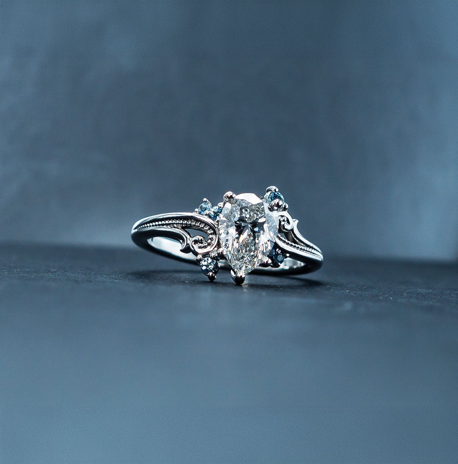 Silver engagement ring with a large clear gemstone on a dark blue background
