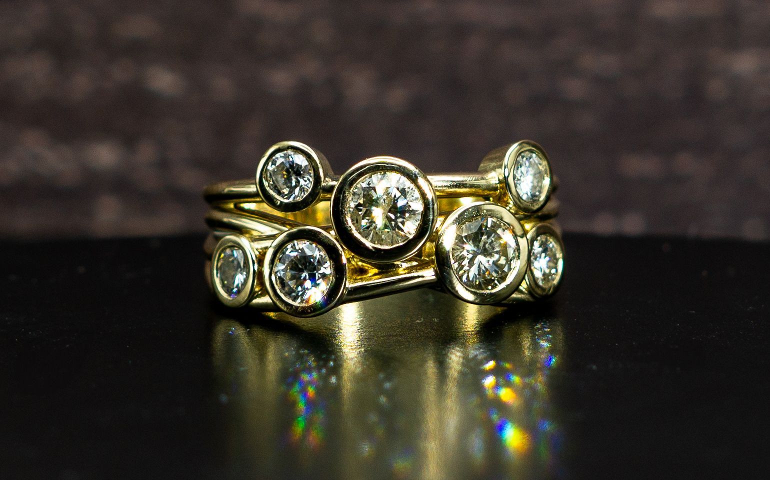 Gold ring with multiple clear gemstones on a glossy dark surface