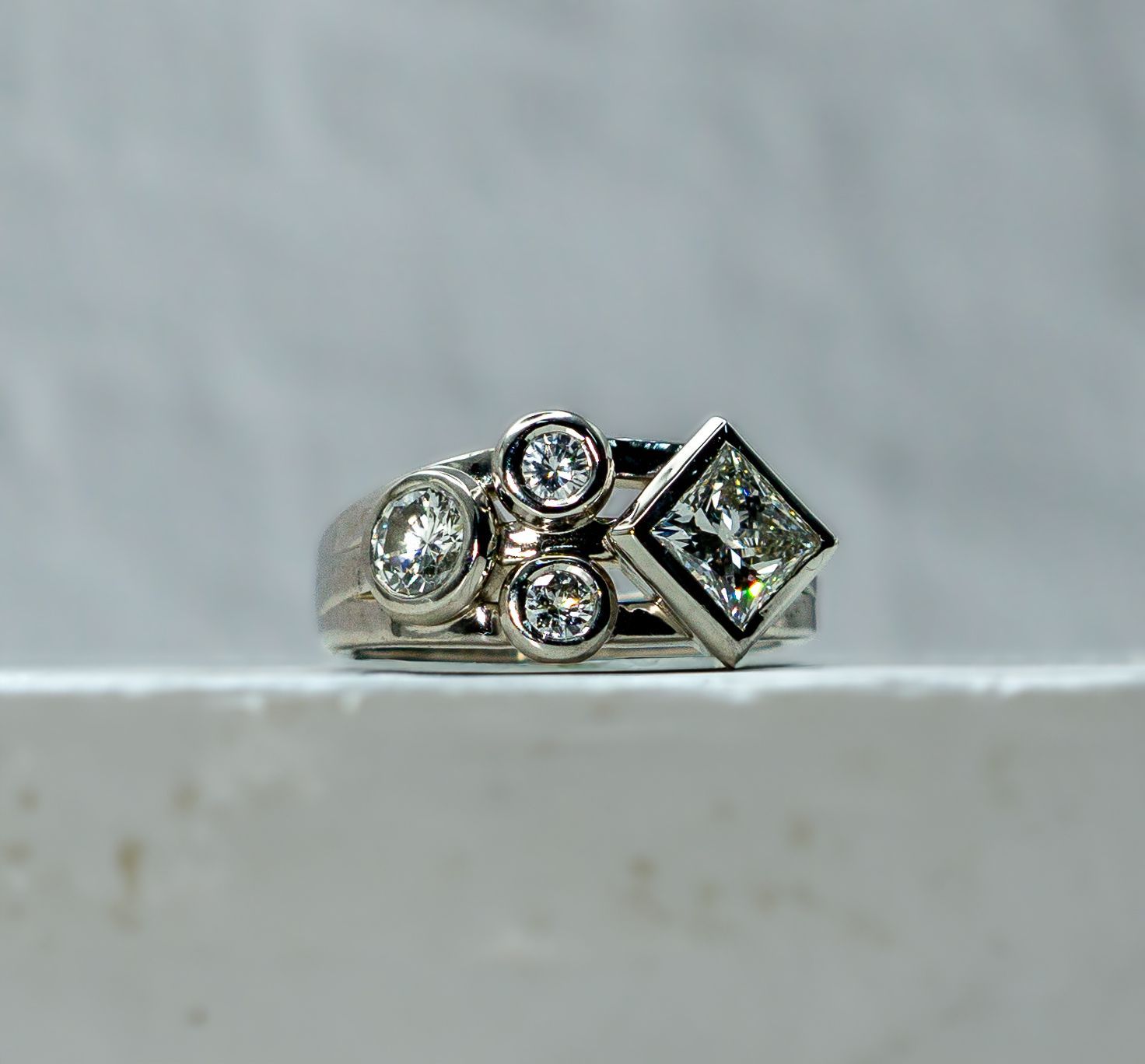 Silver diamond ring with three round stones and one square stone on a light surface