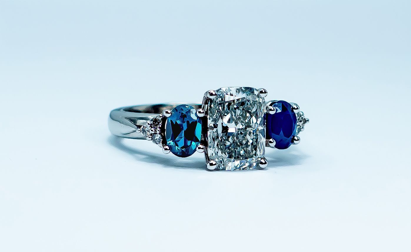 Silver ring with a rectangular clear center stone and blue side stones on a white background
