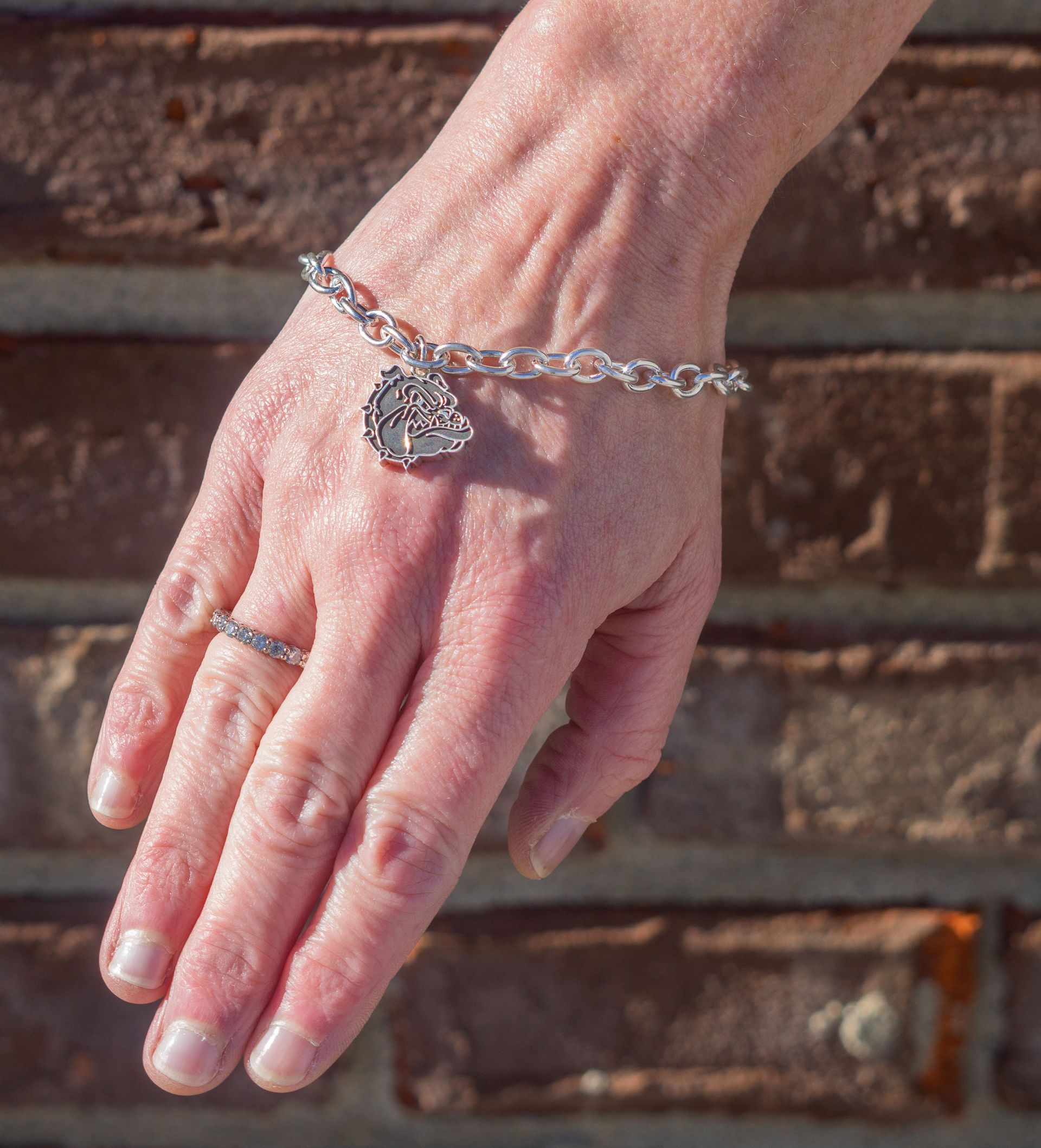 Hand wearing a silver bracelet and ring against a brick wall