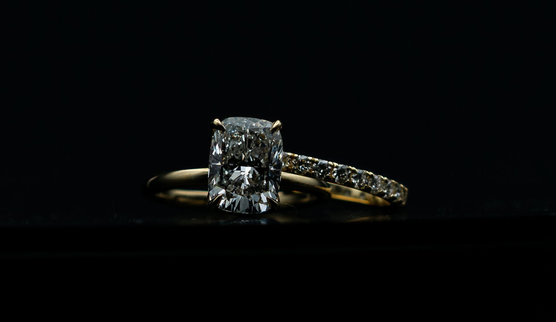 Diamond engagement ring on a black background, with a solitaire center stone and pavé band