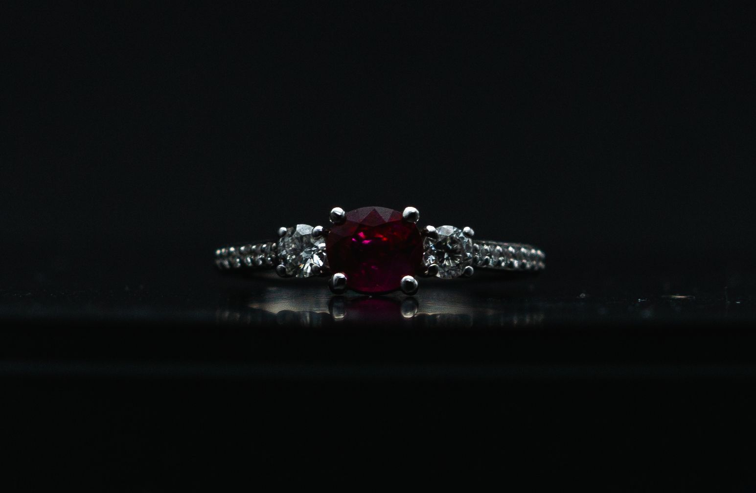 Red gemstone ring with silver band and small diamonds on a dark background