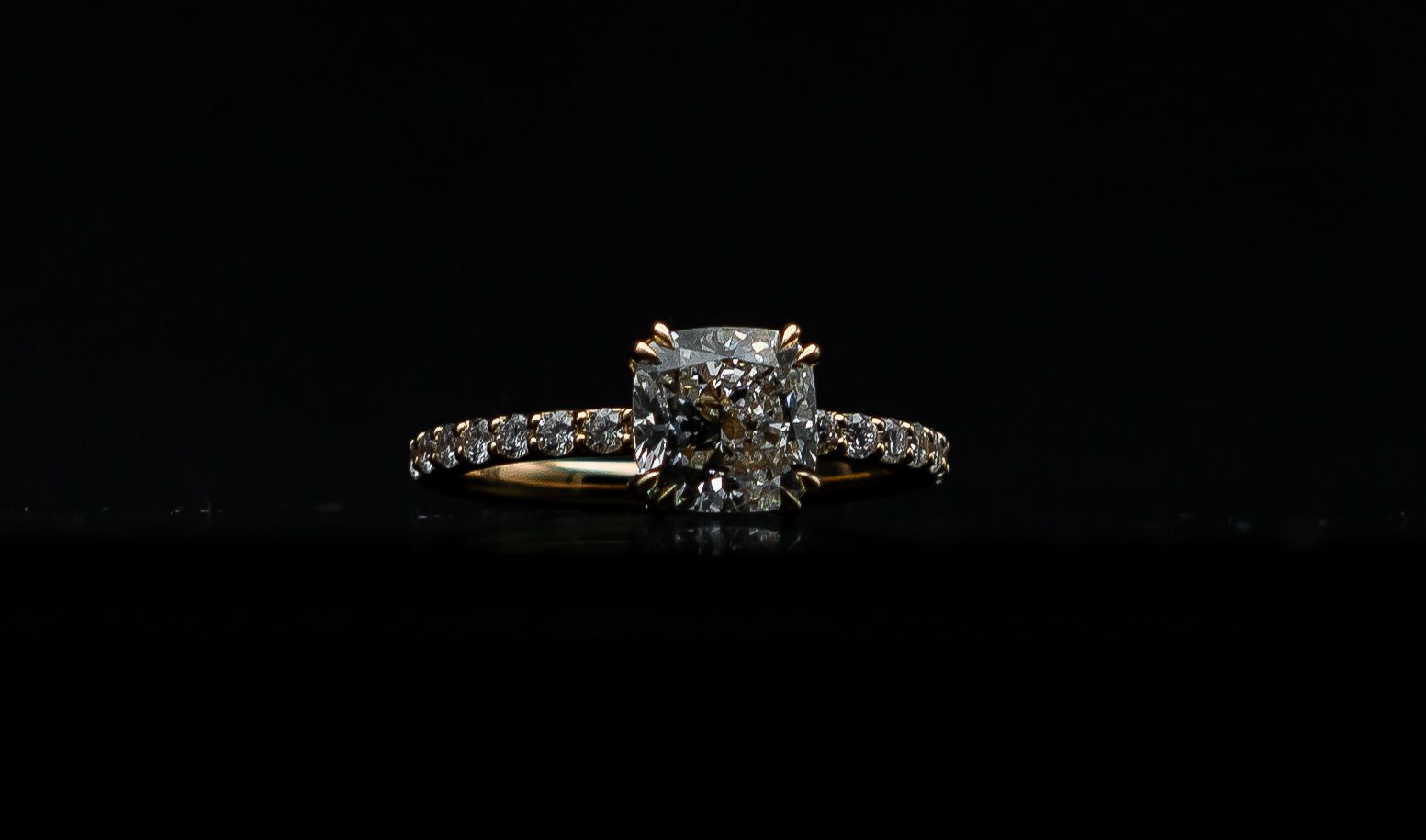 Diamond engagement ring on a black background, with a square center stone and pavé band