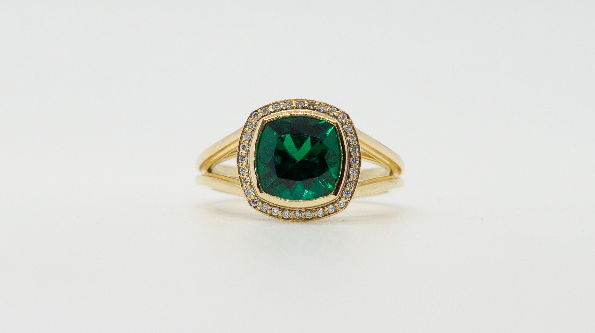 Gold ring with a square green gemstone and small surrounding stones on a white background