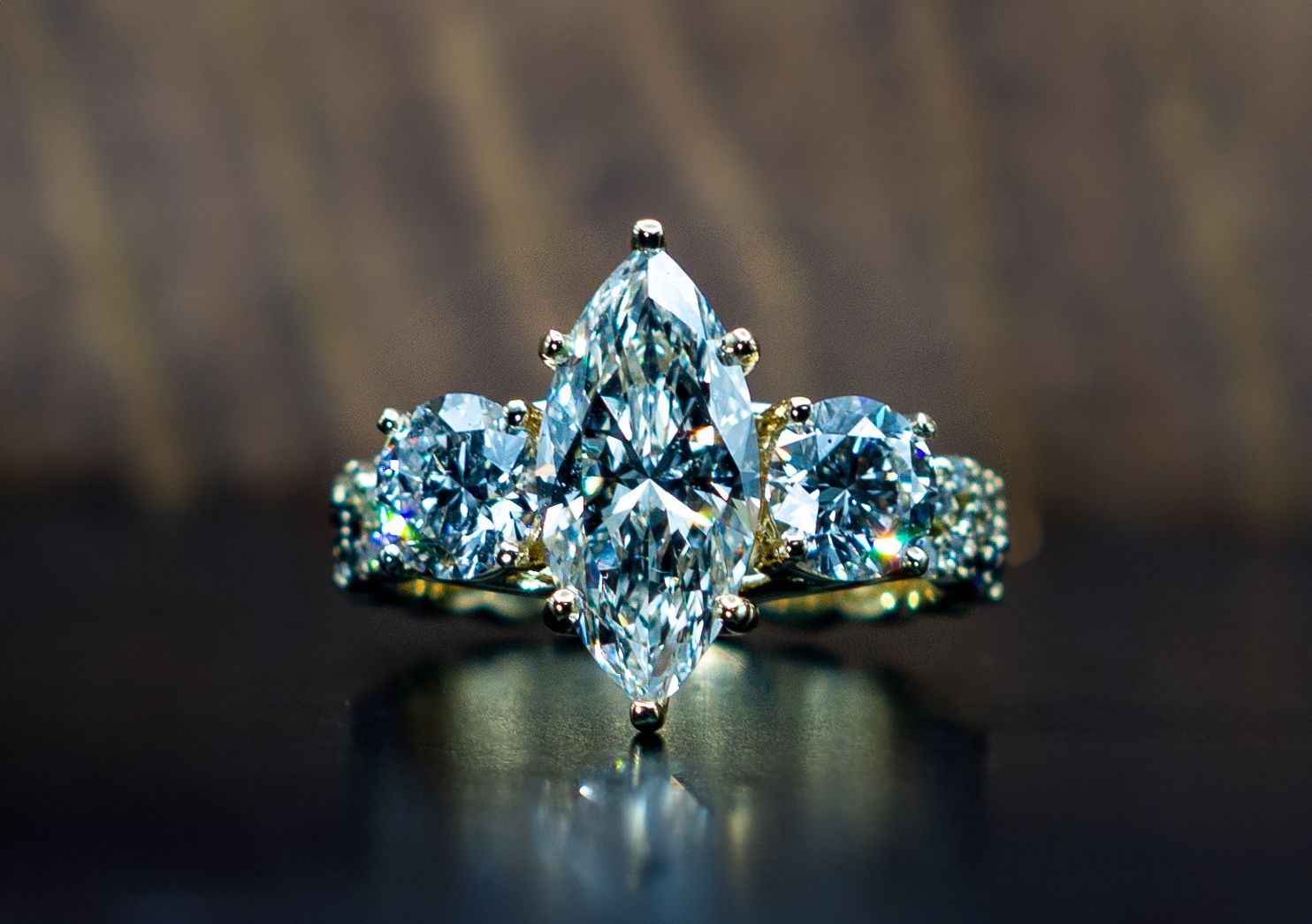 Close-up of a sparkling diamond ring with a large center stone and side stones on a dark surface.