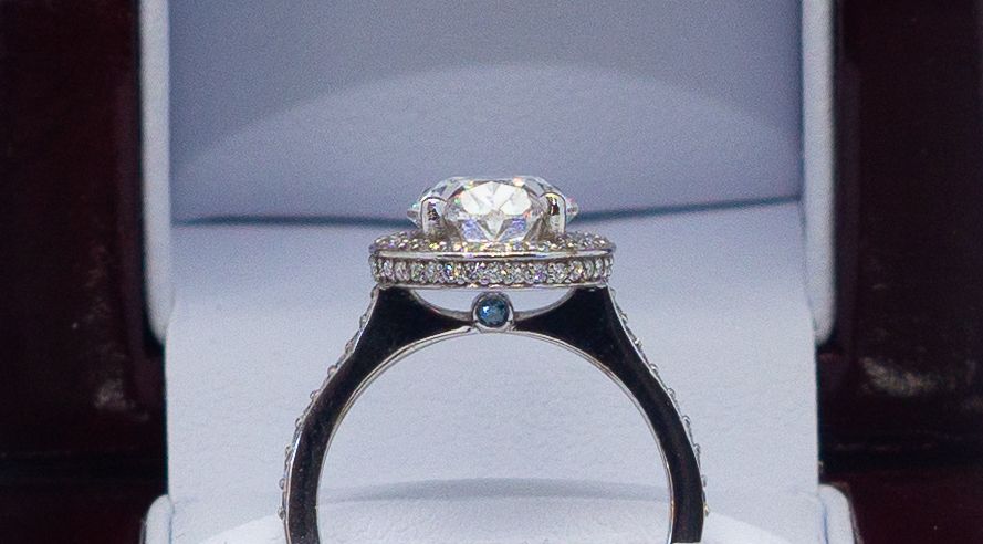 Diamond engagement ring in a white jewelry box, with a blue accent stone on the band