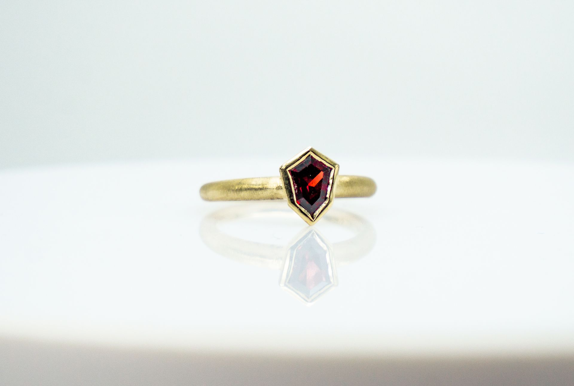 Gold ring with a dark red gemstone on a white reflective surface