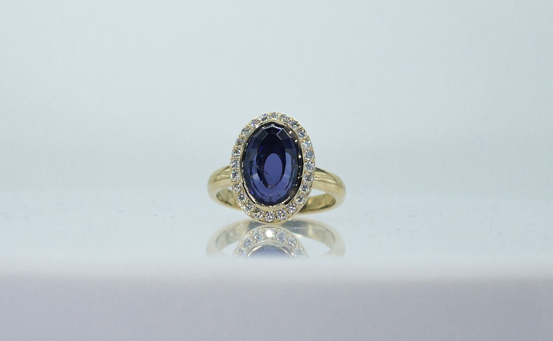 Gold ring with an oval blue gemstone and clear accents on a white background