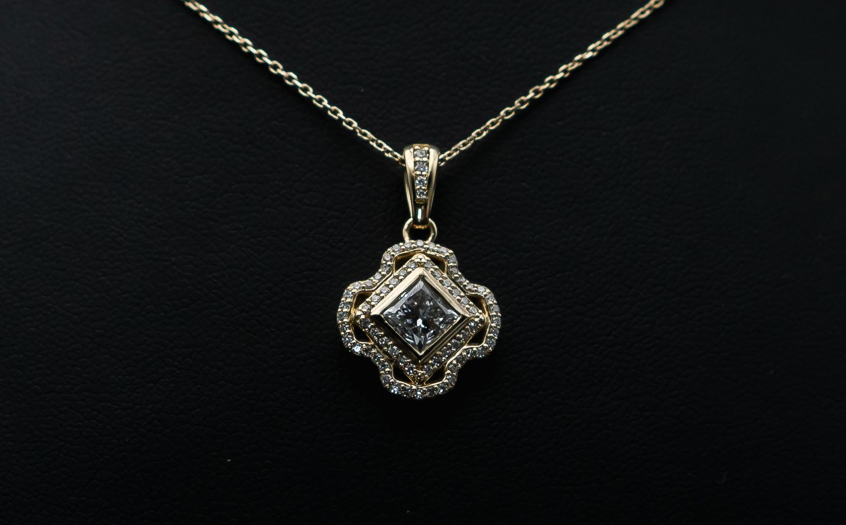 Gold pendant necklace with a square, jeweled charm on a dark background
